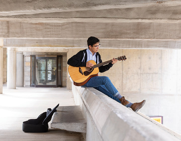 Student playing guitar outside the Humanities building 2019.