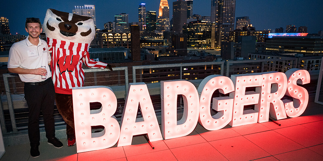 Bucky and an alumnus pose on the roof at night beside the word “BADGERS” lit up with light bulbs.