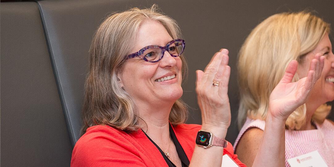 Two alumnae applaud while listening to a speaker.